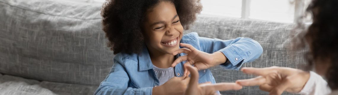 Young girl smiling while signing with an adult